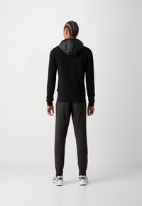 Black knit hoodie with a quilted black hood, paired with dark grey joggers and white sneakers. The outfit has a fitted and casual design.