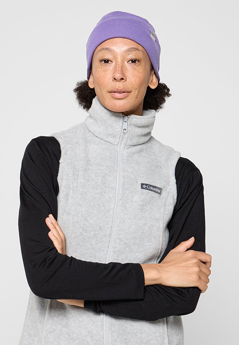 Grå fleece zip-up väst med hög krage, med ett svart långärmat baslager under och en lila stickad mössa på huvudet.