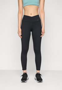 Leggings noirs taille haute avec un design texturé et une ceinture angulaire, associés à des chaussures de sport noires avec des accents blancs.