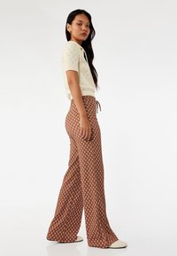 Cremfarbener, gestrickter Kurzarm-Top und braune, gemusterte weit geschnittene Hose mit einem Kordelzugbund. Glatte Textur, dezente Musterung überall.