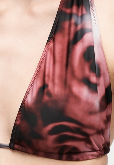 Prim-plan al unei persoane care poartă un top de bikini roșu și negru cu model, confecționat dintr-un material neted și cusături detaliate de-a lungul marginii.