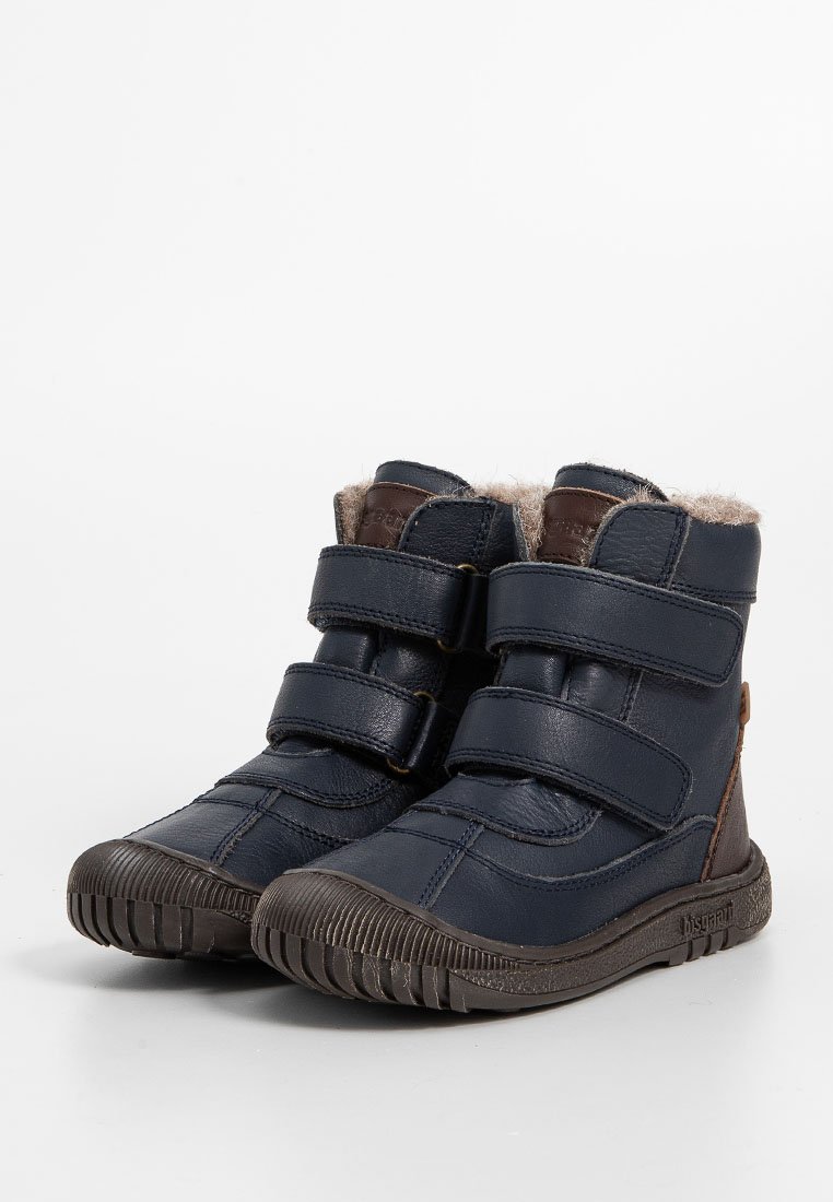 Marineblaue Lederstiefel mit braunen Akzenten, ausgestattet mit zwei Klettverschlüssen, einem Futter aus Fell an der oberen Kante und einer Gummisohle mit strukturiertem Profil.