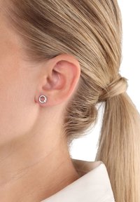 Silver cirkulär studs med en liten pärlaccent, visade på en models öra, med ljust, texturerat hår och en neutral skjorta.