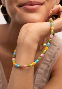 Pulsera de cuentas coloridas con cuentas alargadas y rayadas en rojo, verde, azul, amarillo y naranja, llevada en una mano.