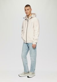 Jasno beżowy hoodie z zamkiem błyskawicznym, z kapturem na sznurki, bocznymi kieszeniami, zestawiony z jasnoniebieskimi dżinsami i jasnoszarymi trampkami.