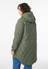 Zaļa olīvu krāsas pūsta jaka ar kapuci, kurai ir izliekta izšūšanas raksts. Garš ar aprocēm piedurknēs un noapaļu apakšmalu.