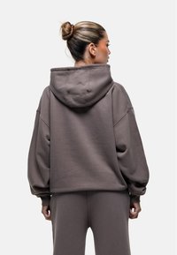 Oversized, hoodie in donkergrijs stof. Heeft verlaagde schouders, ribgebreide manchetten en een gladde textuur. Achteraanzicht weergegeven.
