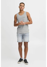 Top din bumbac gri, cu un mic buzunar și un design brodat, purtat cu pantaloni scurți din denim deschis, răsuciți la manșete, și adidași negri.