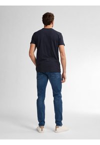Camiseta de algodón azul marino con mangas cortas, combinada con jeans de denim azul claro y zapatillas beige, vista trasera.