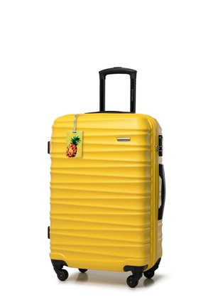 Yellow hard-shell luggage with ribbed texture, black wheels, retractable handle, and a pineapple-themed luggage tag.