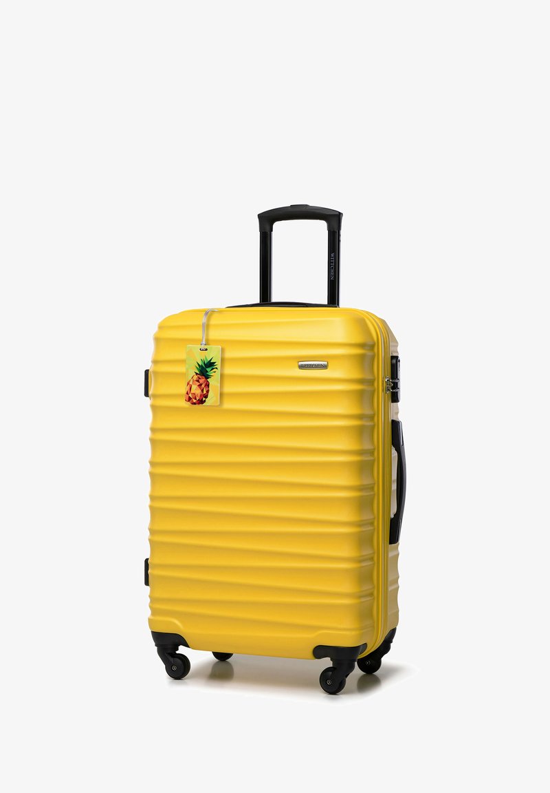 Žlutý kufr s tvrdým krunýřem a vroubkovanou texturou, černá kola, vysouvací rukojeť a zavazadlová visačka s motivem ananasu.