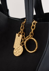 Black leather handbag with gold chain featuring a hammered textured ring and two decorative gold pendants attached to the handle.