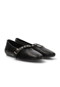 Zapatos planos negros con punta afilada, hechos de cuero suave. Presentan una correa con tachuelas decorativas y un detalle de hebilla en el lateral.