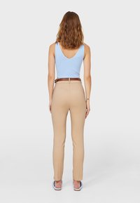 Jasnoniebieski bezrękawnik z dekoltem w serek, zestawiony z beżowymi dopasowanymi spodniami i brązowym paskiem, prezentujący gładką tkaninę i dopasowany krój.