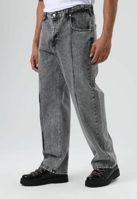 Grijze denim jeans met een losse pasvorm, voorzien van een rechte snit, zichtbare stiksels en zijzakken. Gecombineerd met zwarte veterlaarzen.