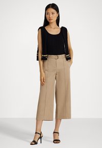 Black cable-knit tank top paired with high-waisted, wide-leg beige trousers. Model wears black strappy heels. Simple design, no patterns.