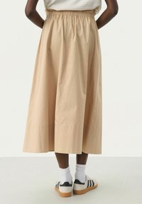 Light beige midi skirt with an elastic waistband, featuring a smooth texture and subtle draping. Paired with white socks and casual shoes.