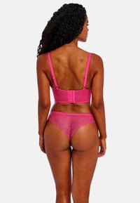 Růžový krajkový komplety spodního prádla, který zahrnuje podprsenku s nastavovacími ramínky a háčkovým zapínáním, a odpovídající krajkové kalhotky s vlnitými okraji.