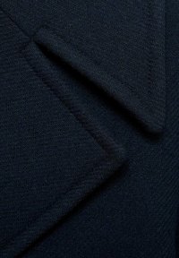 Tissu bleu marine foncé avec un motif chevrons subtil, plié en diagonale montrant la texture et l'épaisseur.