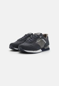 Zapatos deportivos de color gris oscuro, hechos de ante y malla, con una parte superior texturizada, cierre de cordones y media suela de espuma blanca. Los detalles incluyen la marca.