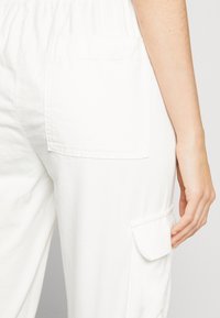 Witte katoenen broek met een zijvak en een achterzak. De stof is glad, met een licht ontspannen pasvorm en een elastische tailleband.