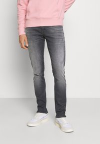 Šedé džíny v slim fit, s mírně vybledlou texturou. V kombinaci s bílými a světle šedými teniskami a růžovou mikinou.