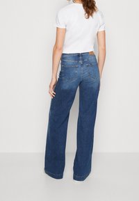 Laadukkaat siniset farkut leveällä lahkeella, joissa on haalistunut pesu, kaksi takataskua ja nahkainen logopatch vyötäröllä.