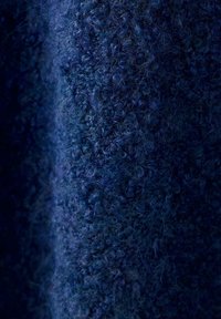Gros plan d'un tissu en laine bleu foncé avec des fibres denses et bouclées et une surface texturée.
