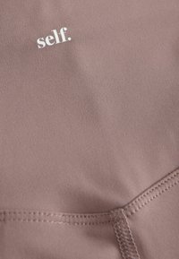 Tessuto morbido e texturizzato in malva tenue con logo "self." bianco. Presenta cuciture minime e una finitura liscia, ideale per l'abbigliamento sportivo.