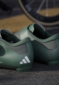 Green athletic shoes with a textured finish, featuring a snug fit and a white three-stripe logo on the side. Robust sole design.