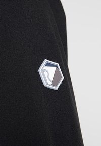 Patch hexagonal avec des formes abstraites en blanc, gris et bleu marine sur un fond en tissu noir texturé.