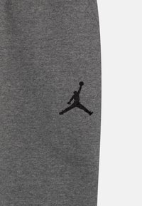 Szare dresy wykonane z tkaniny mieszanki bawełnianej, z czarnym haftowanym logo Jumpman na lewej udzie. Gładka faktura, elastyczny pasek w talii.
