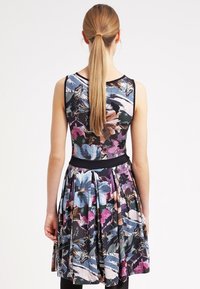 La robe à imprimé floral présente un corsage ajusté, une jupe évasée, des bordures noires à la taille et un mélange vibrant de tons bleu, rose et vert.