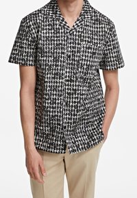 Maglietta a maniche corte in bianco e nero con un motivo geometrico, dotata di colletto e chiusura a bottoni frontale. Realizzata in tessuto leggero.