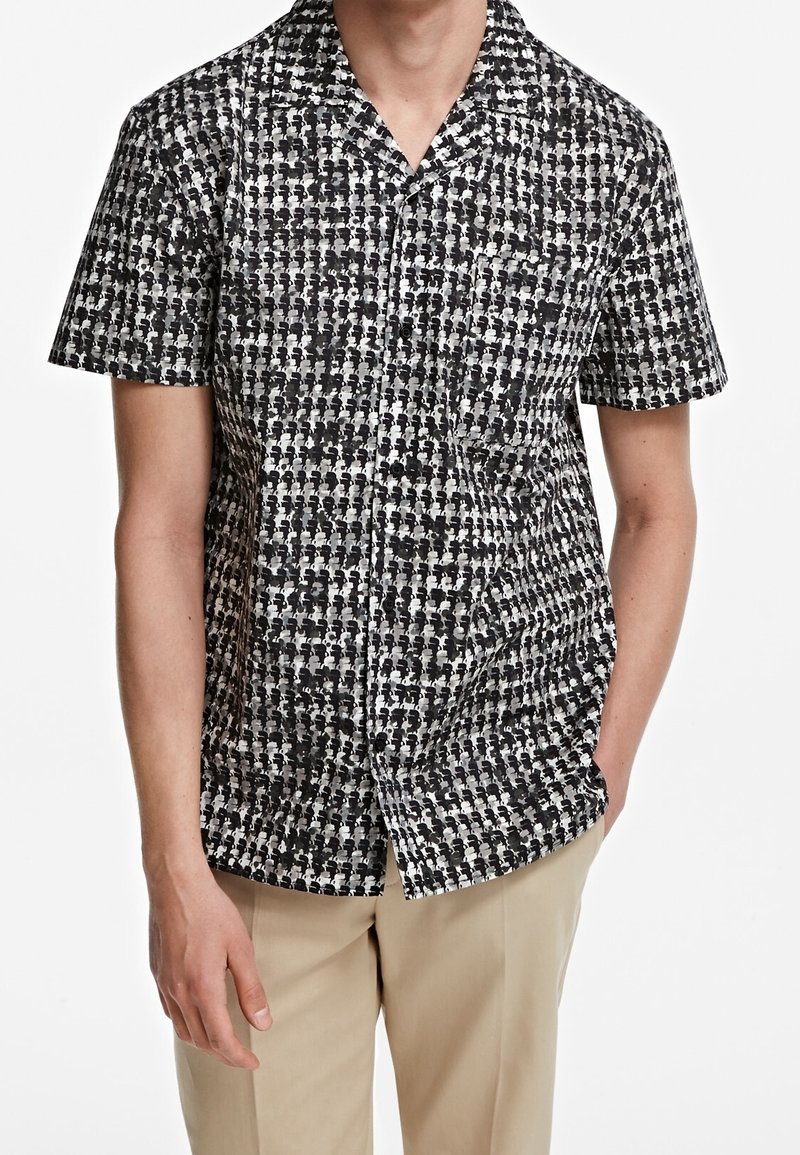 Maglietta a maniche corte in bianco e nero con un motivo geometrico, dotata di colletto e chiusura a bottoni frontale. Realizzata in tessuto leggero.