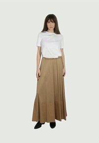 Maglietta bianca e gonna lunga color beige con fascia elastica in vita, tessuto morbido, silhouette ampia, indossata con calzature nere.