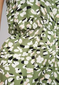 Roheline kangas, millel on musta, valge ja roosa abstraktne print, sujuva tekstuuriga; kogutud vöökoht ja voolav disain.