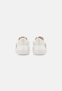 White sneakers with a smooth finish, rounded back, and decorative accents, featuring a textured sole and minimalistic design.