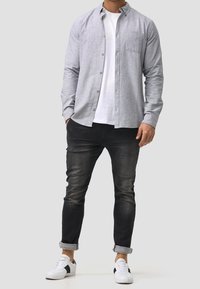 Szara koszula na guziki z długim rękawem, pod nią biała koszulka z okrągłym dekoltem, czarne wąskie dżinsy oraz białe trampki z czarnymi akcentami.