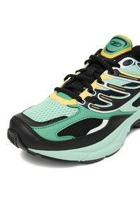 Teniska s vrchnou časťou z oka a syntetického materiálu v mätovo zelenej farbe, čiernymi akcentmi, žltými detailmi a zakriveným dizajnom podrážky s textúrovaným gripom.