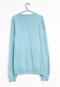 Pull bleu clair à coupe décontractée, col et poignets côtelés, manches longues et texture en tricot lisse. Suspendu à un crochet noir.