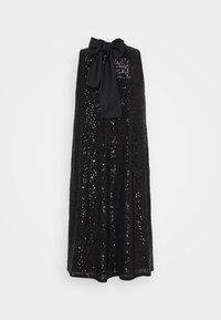 Robe noire sans manches couverte de sequins avec un grand nœud noir noué au col haut sur un fond uni.