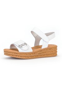 White leather sandal with a wide strap and adjustable back, featuring a silver accent, set on a textured cork wedge sole.