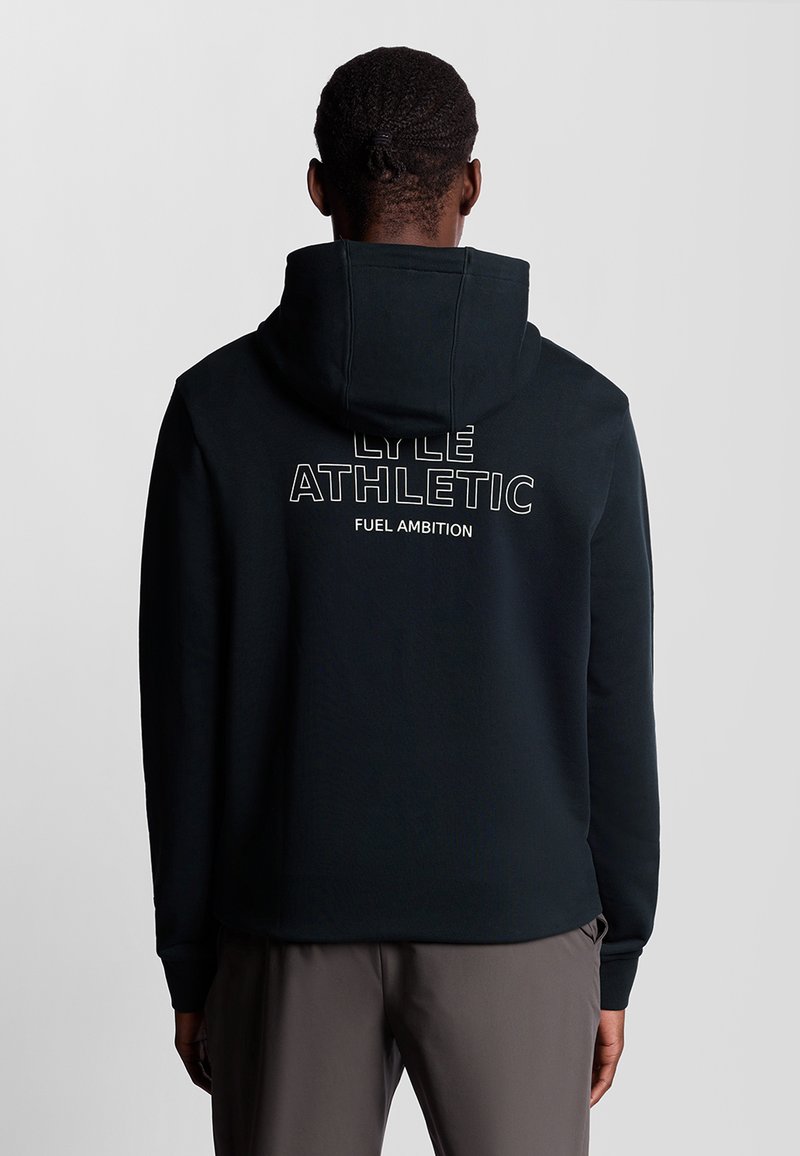 Schwarzer Kapuzenpullover aus weichem Stoff, mit dem Aufdruck "LYLE ATHLETIC FUEL AMBITION" in Weiß auf dem Rücken. Glatte Textur, minimalistisches Design.