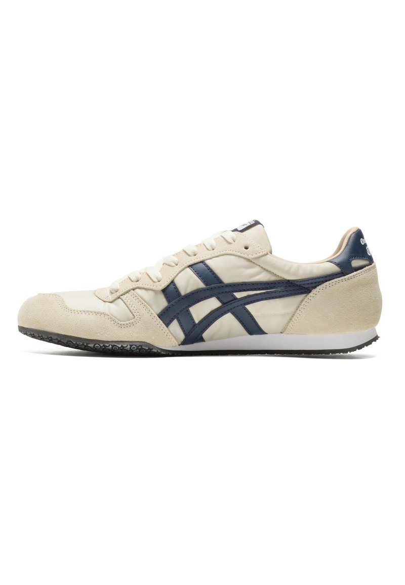 Scarpa atletica beige con accenti in pelle blu navy, puntale in suede e suola in gomma nera con un motivo testurizzato.