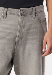 Jeans de denim gris con un corte recto. Las características incluyen un cierre de botón, diseño de cinco bolsillos y un ligero desgaste en la tela.