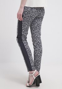 Sittande byxor i svart och vitt mönster med geometrisk design, med en enfärgad svart sidopanel och slank fåll, kombinerat med klackar.