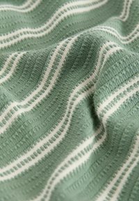 Weicher grüner Strickstoff mit erhabenen weißen Streifen, die horizontal über die Oberfläche verlaufen.