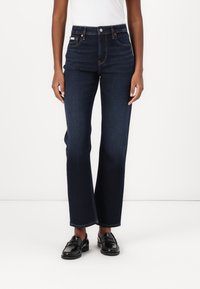 Jeans de talle alto azul oscuro con una silueta de pierna recta. Presentan un diseño de cinco bolsillos y costuras en contraste. Llevados con mocasines negros.