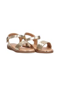 Sandalias metálicas doradas con diseño floral recortado, tira ajustable en el tobillo, suela plana y textura suave. Adecuadas para el uso en climas cálidos.
